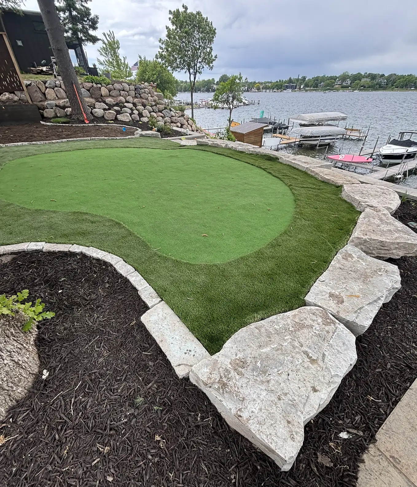 Lakeside artificial turf putting green with natural boulder edging at Lake Minnetonka property