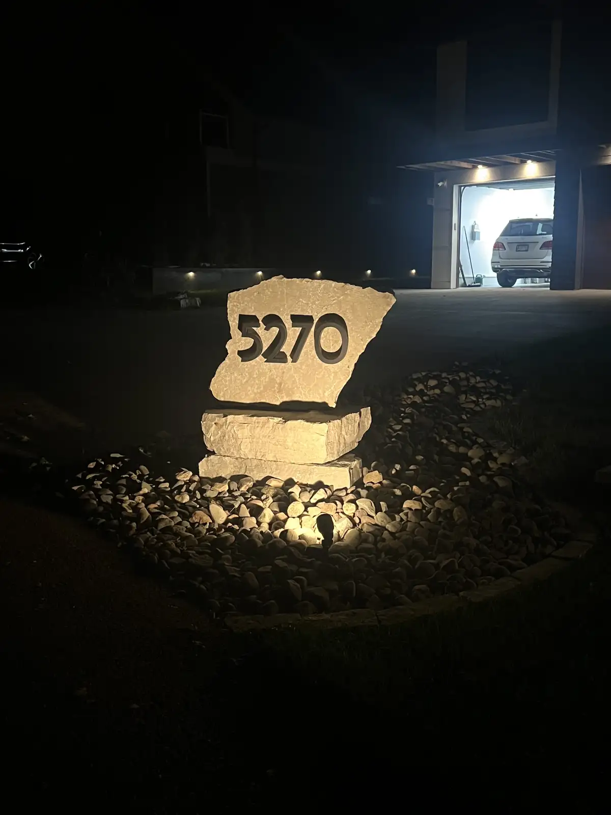 Custom landscape lighting illuminating stone address marker at night