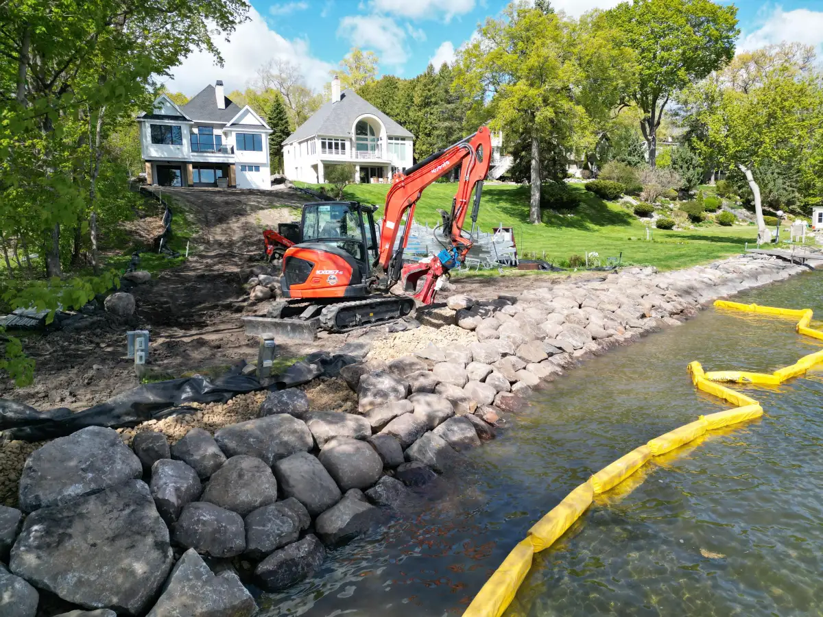 Excavator placing large fieldstone boulders for lakeshore rip rap stabilization on Lake Minnetonka